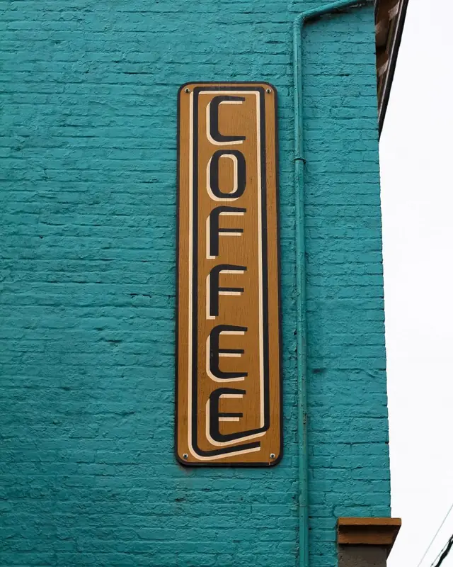 A vertical brass COFFEE blade sign on a teal brick wall